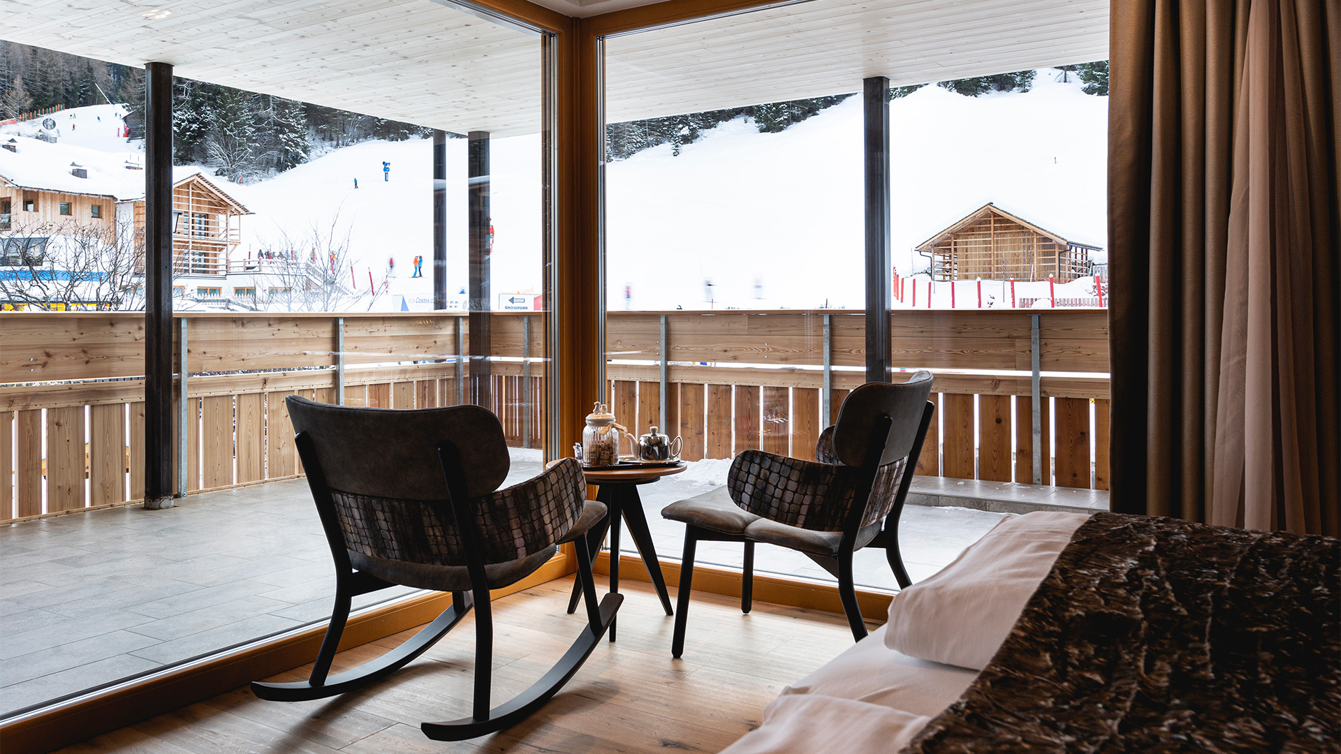 Gemütliche Ecke eines Alpine-Zimmers mit zwei Holzstühlen und Panoramablick auf die verschneiten Dolomiten.