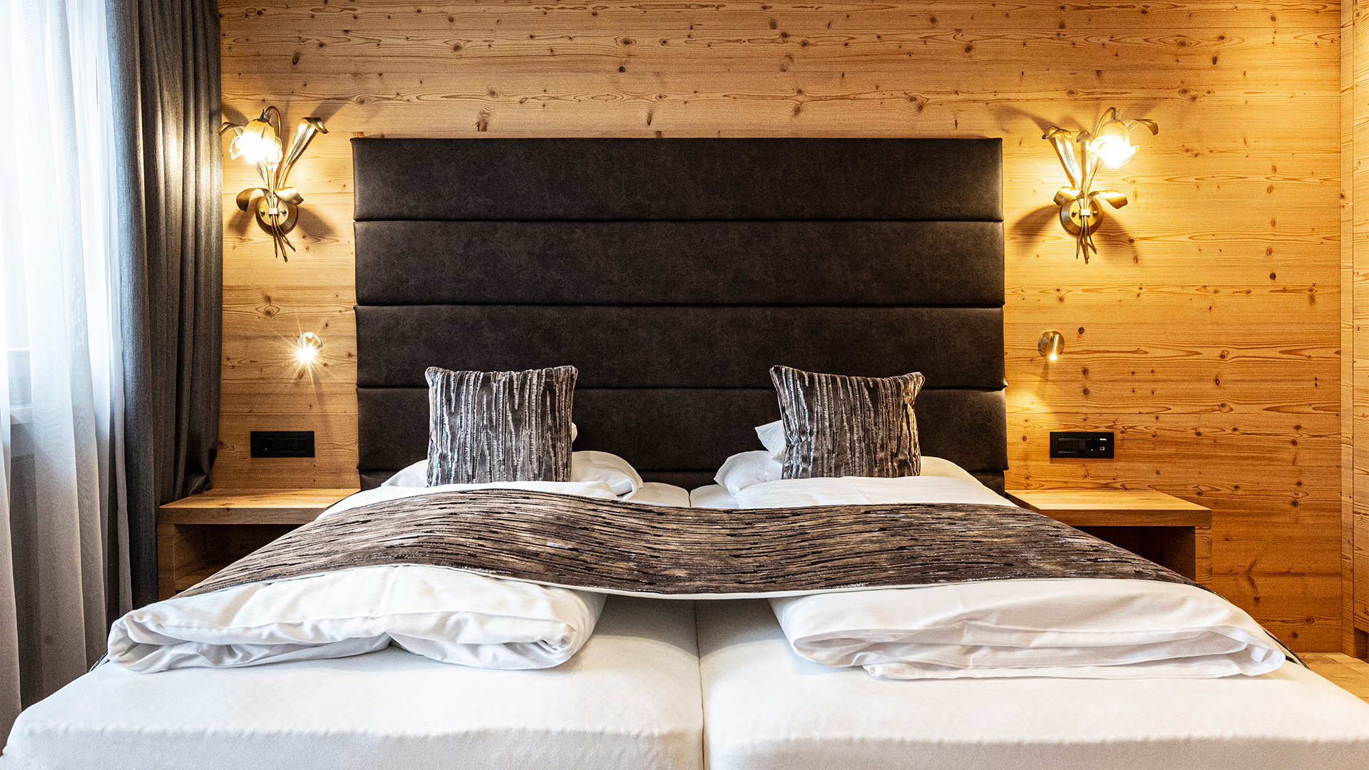 Doppelbett im alpinen Stil mit dunklem gepolstertem Kopfteil, Holzwand, Leselampen und weißer Bettwäsche