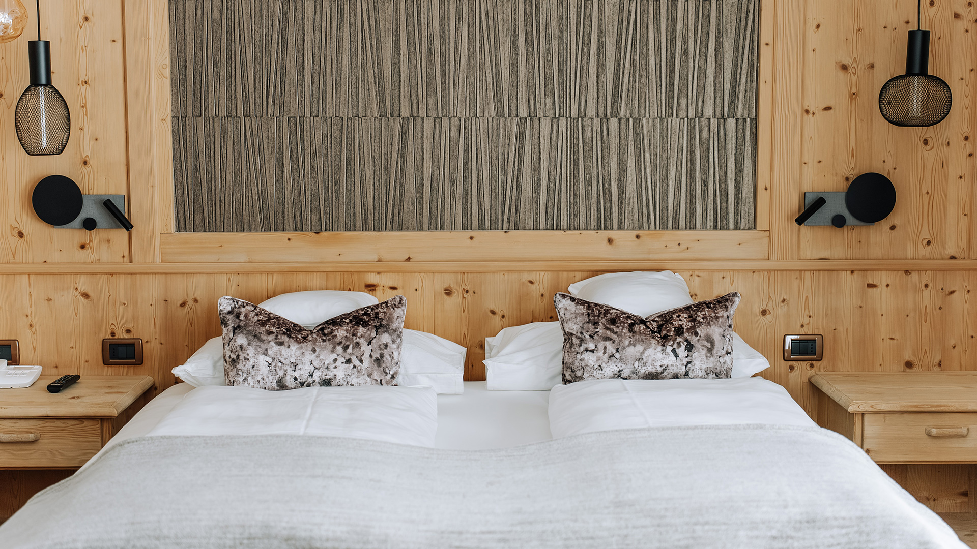 Elegantes Schlafzimmer im Hotel Arkadia mit warmen Holzwänden, makellosen Betten, Designerlampen und einem dekorativen Paneel.