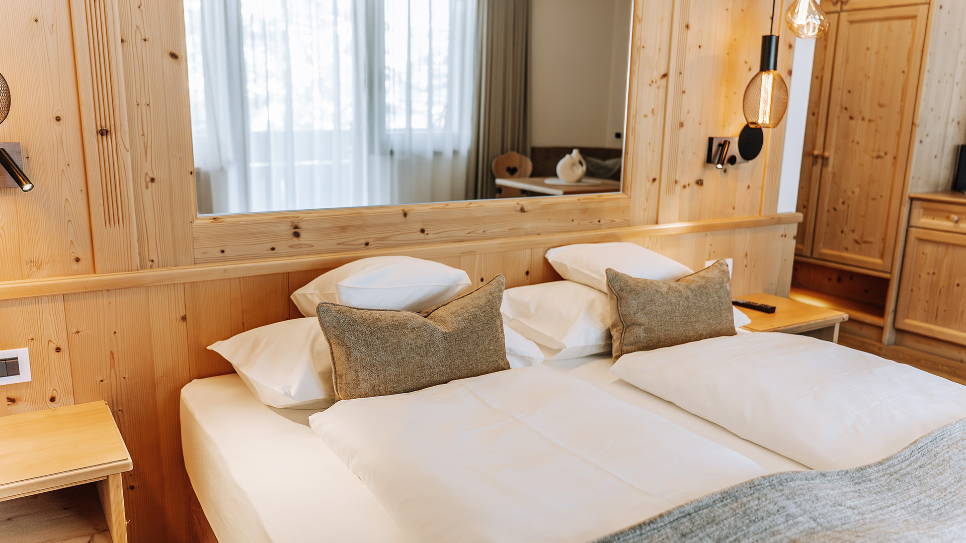 Elegantes Comfort Plus Zimmer im Hotel Arkadia mit weißen Laken und hellen Holzpaneelen, natürliches Licht für Komfort und Stil in den Dolomiten.
