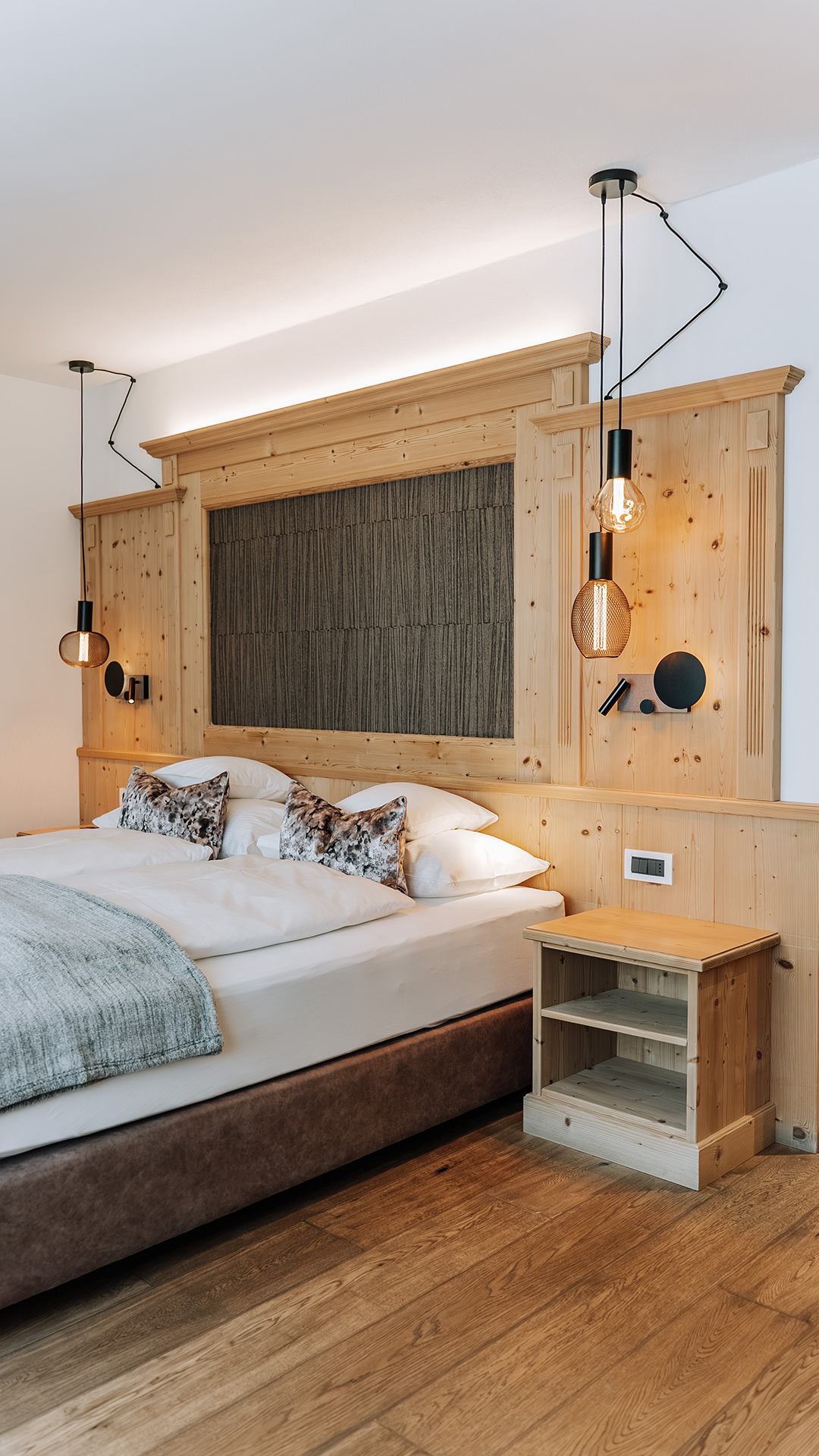 Komfort Plus Zimmer mit hellen Holzmöbeln, dekorativem Kopfteil und warmer Beleuchtung