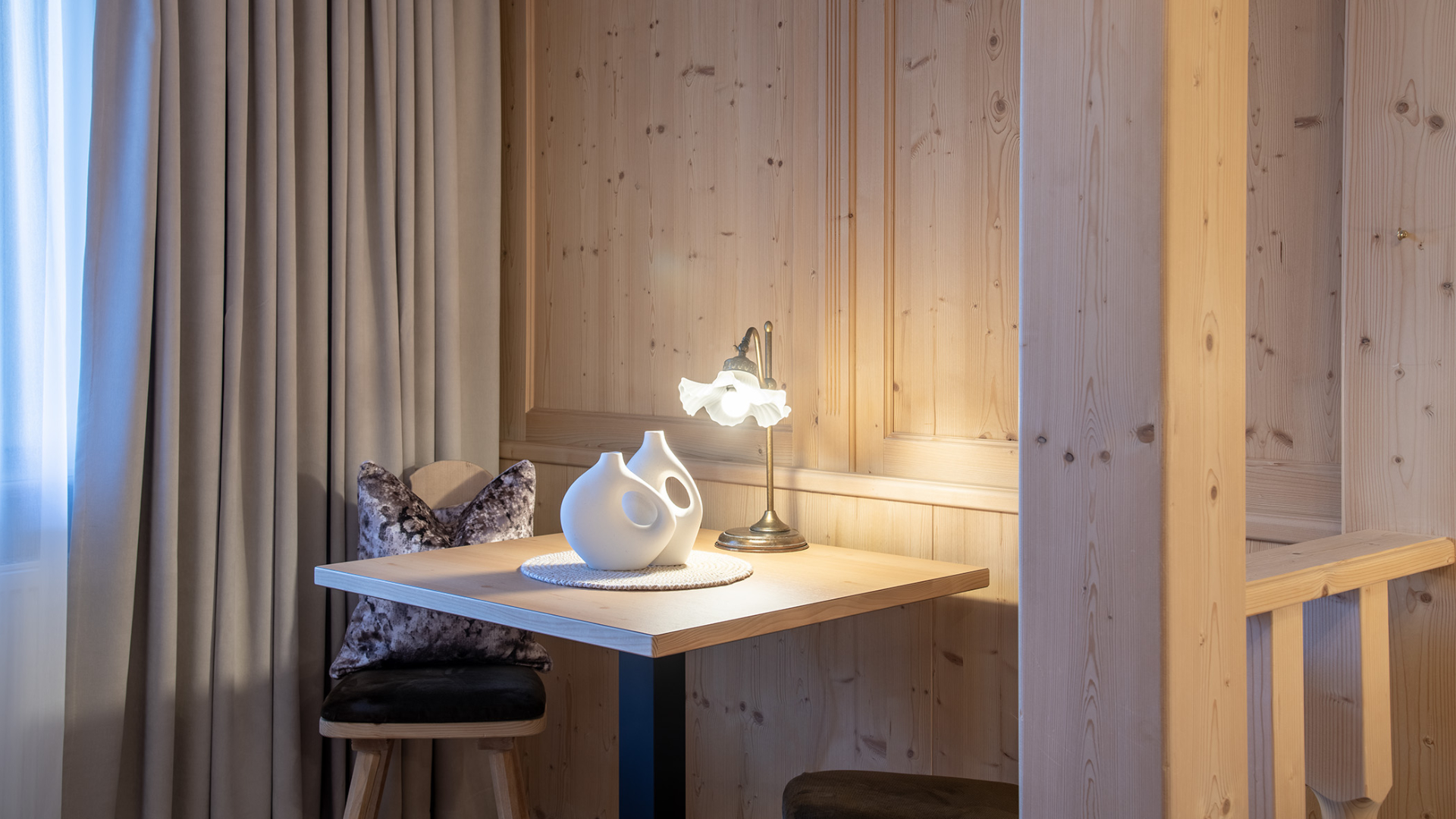 Gemütliche Entspannungsecke des Komfortzimmers mit Tisch, Stuhl und Holzverkleidung.