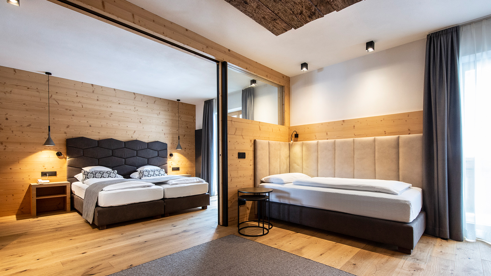 Gemütliches Zimmer des Hotel Arkadia mit Holzwänden, natürlichem Licht, Parkettboden und grauem Teppich