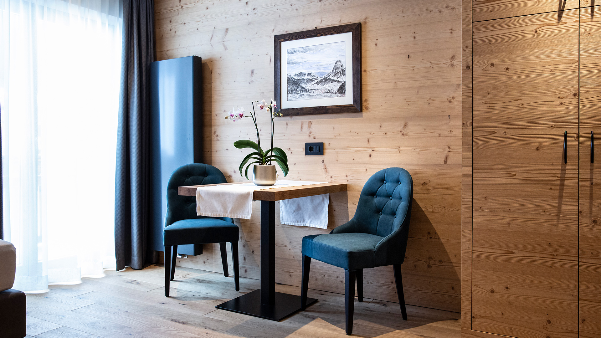 Gemütliche Lounge-Ecke einer Junior Suite des Hotel Arkadia mit blauen Sesseln, Tisch und Holzwänden.