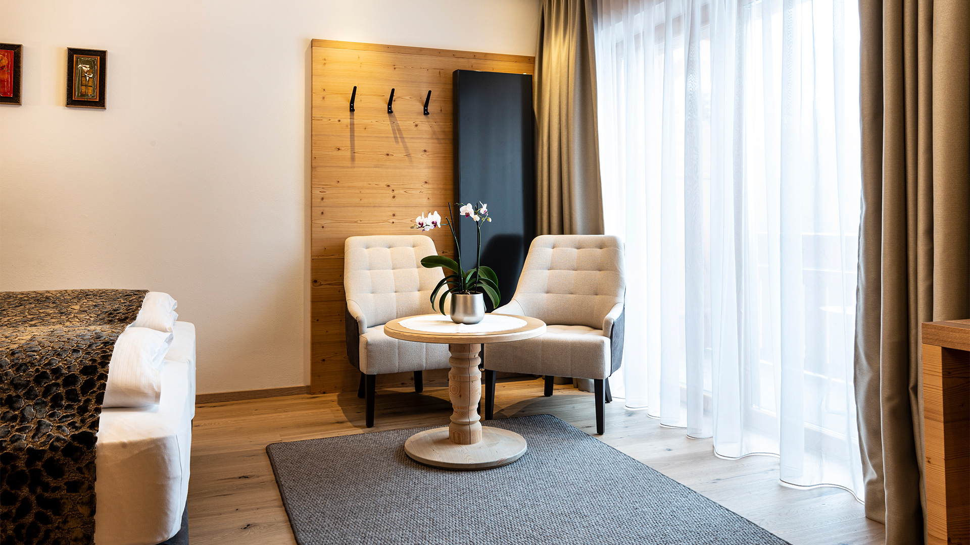 Entspannungsecke der Junior Suite mit zwei gepolsterten Sesseln, rundem Beistelltisch mit Orchidee und großen hellen Vorhängen.