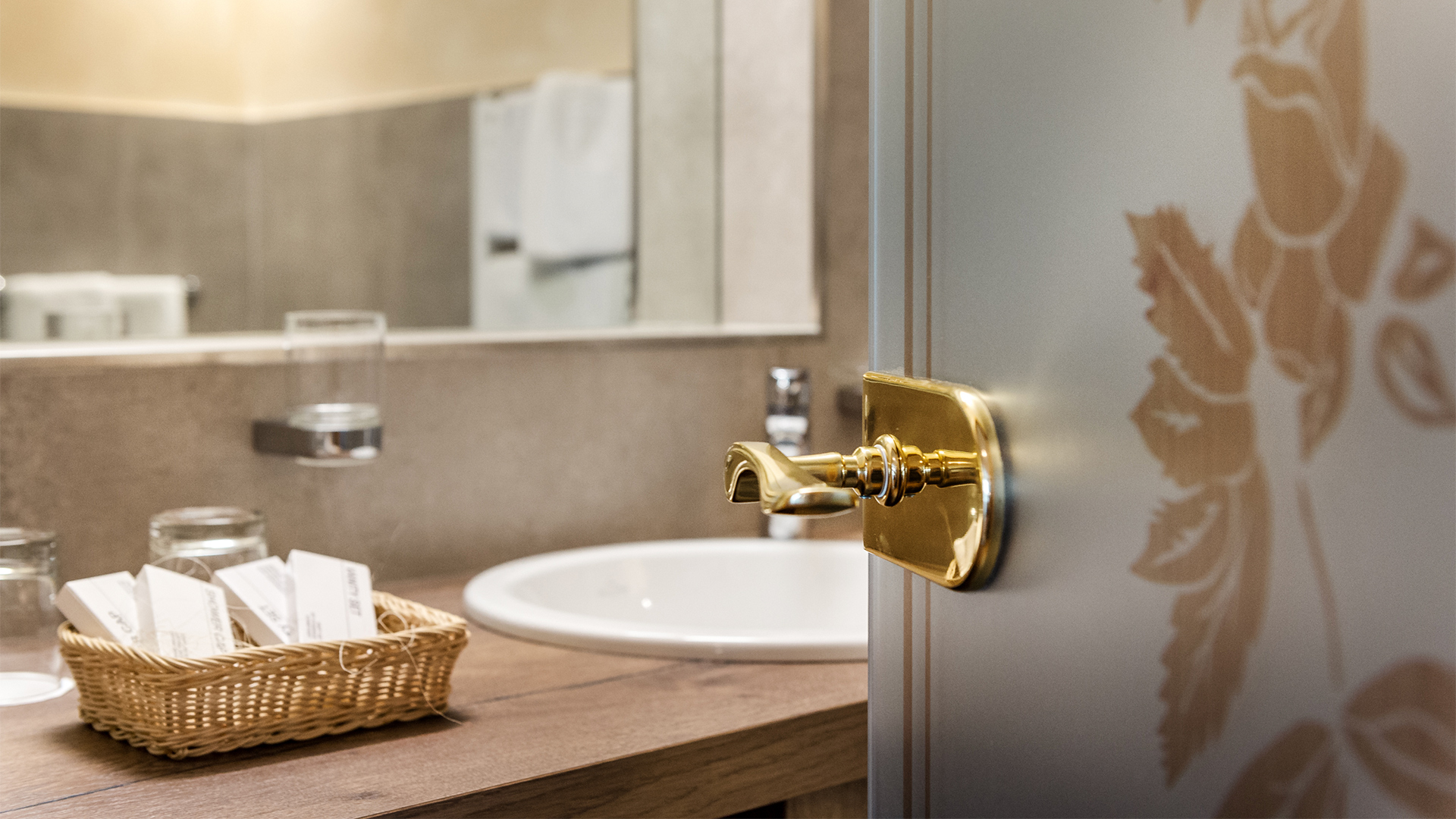 Badezimmer mit Waschbecken, Spiegel, Tür mit goldenem Griff und Pflegeprodukten