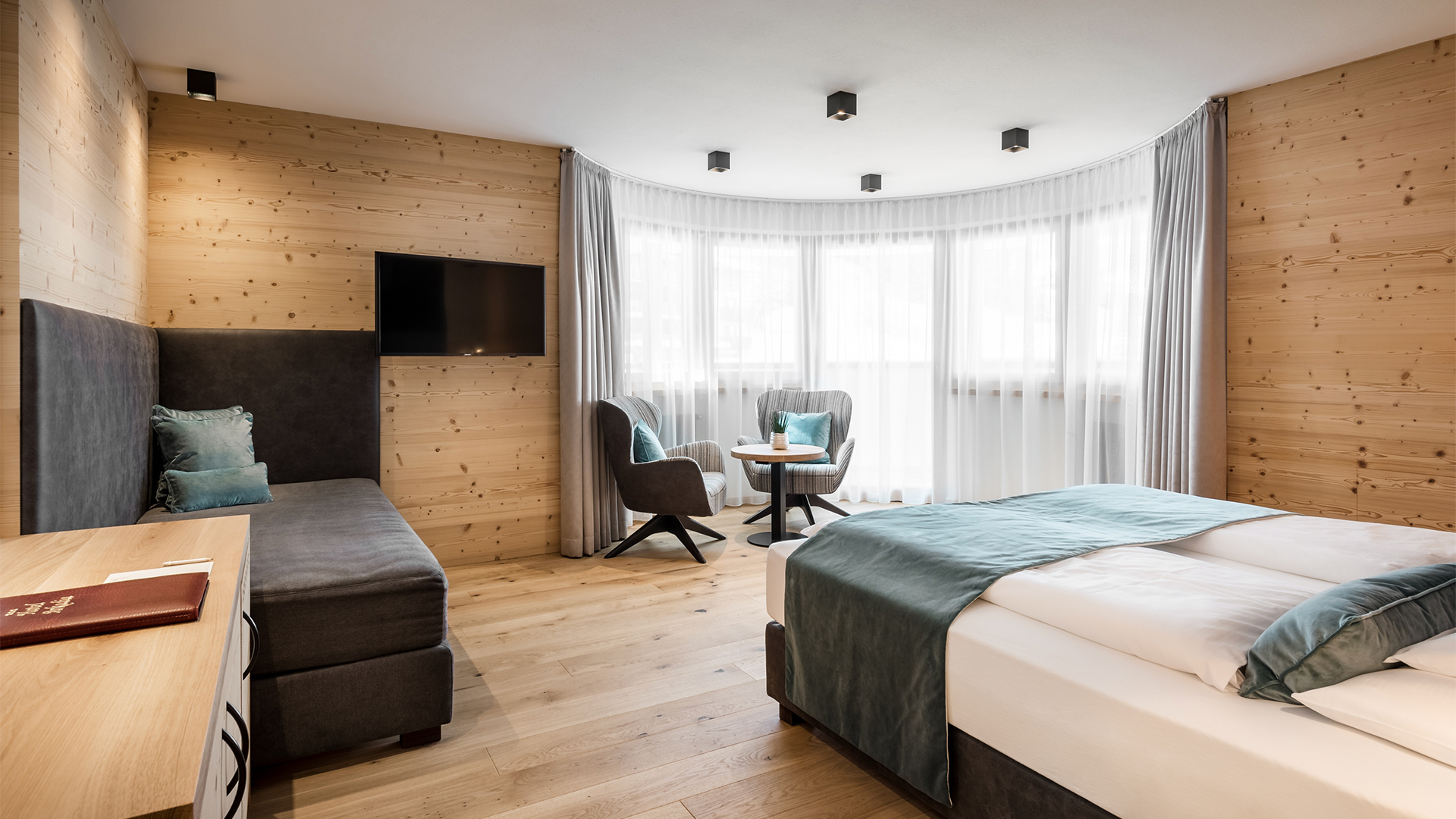 Gemütliches und geräumiges Tor-Zimmer des Hotel Arkadia mit Holzwänden, hellen Fenstern, Zwischengeschoss und Entspannungsecke.