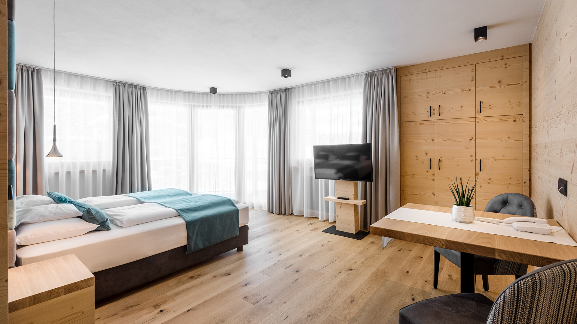 Geräumiges Tor-Zimmer des Hotel Arkadia: helle Holzwände, große Fenster, bequeme Betten und ein Wohnbereich mit Tisch und Stühlen