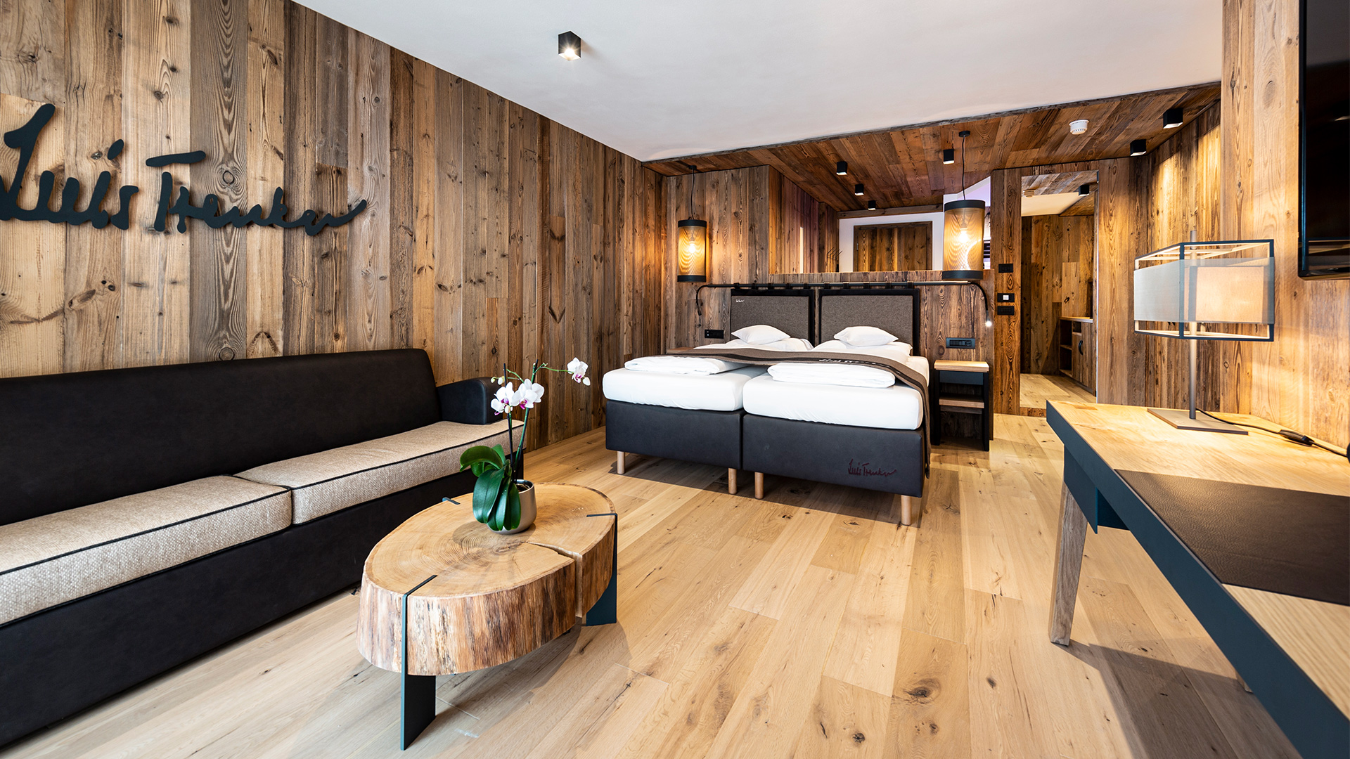 Trenker Zimmer aus Holz mit Wohnbereich, Sofa, Doppelbett und Schreibtisch