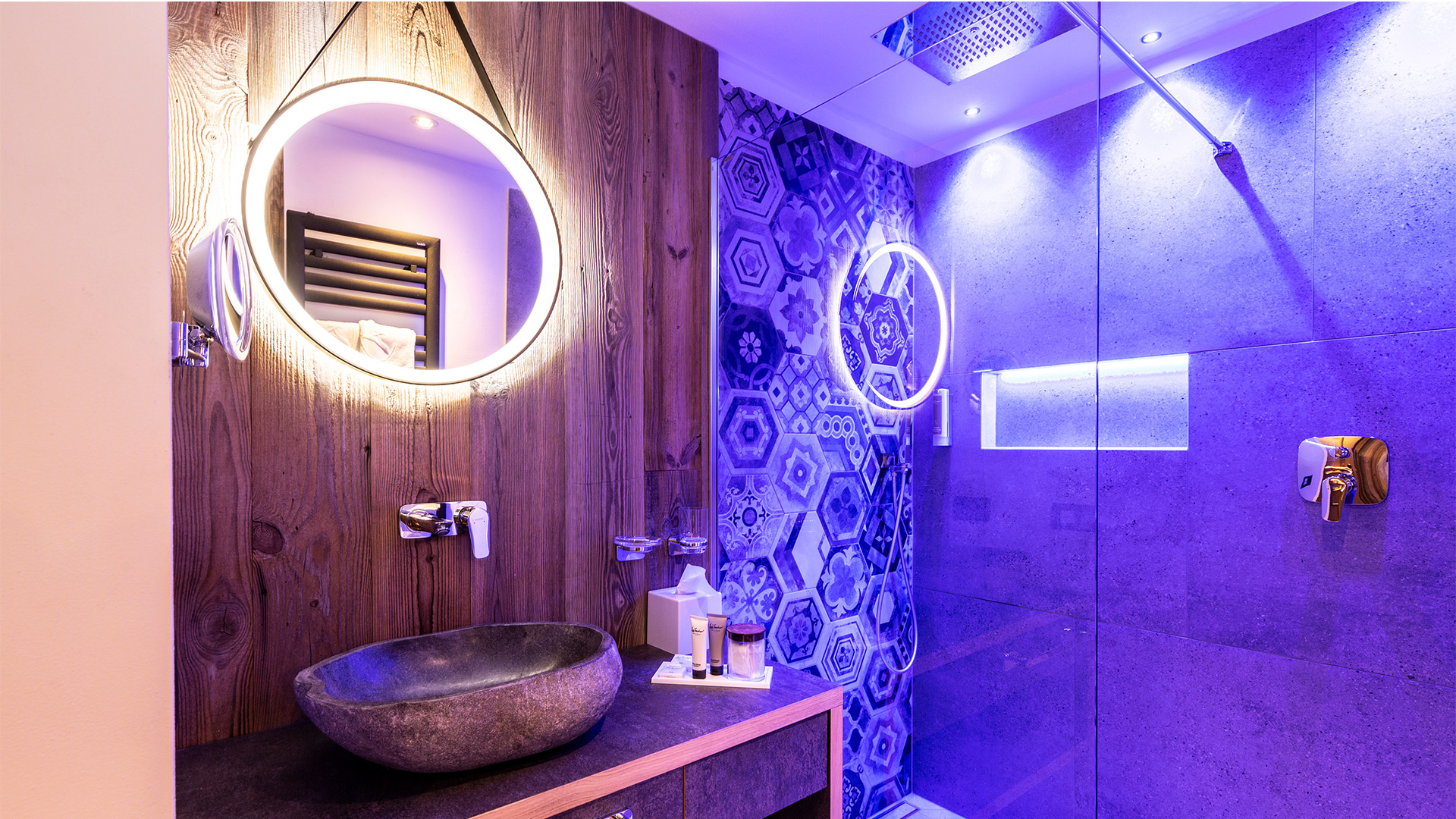 Modernes Badezimmer Hotel Arkadia: sanfte violette Beleuchtung, blau-graue Fliesen, Steinwaschbecken und graue Ablagen.